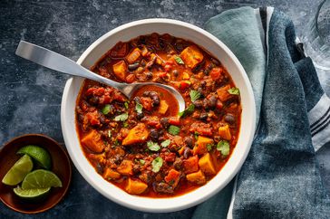 Sweet potato & black bean chili in a white bowl with a spoon in it. Lime wedges on the side and fresh cilantro sprinkled on top