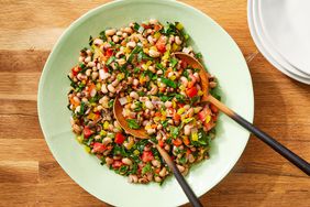Spicy black-eyed pea & collard green salad in a light green bowl with two wooden servings spoons