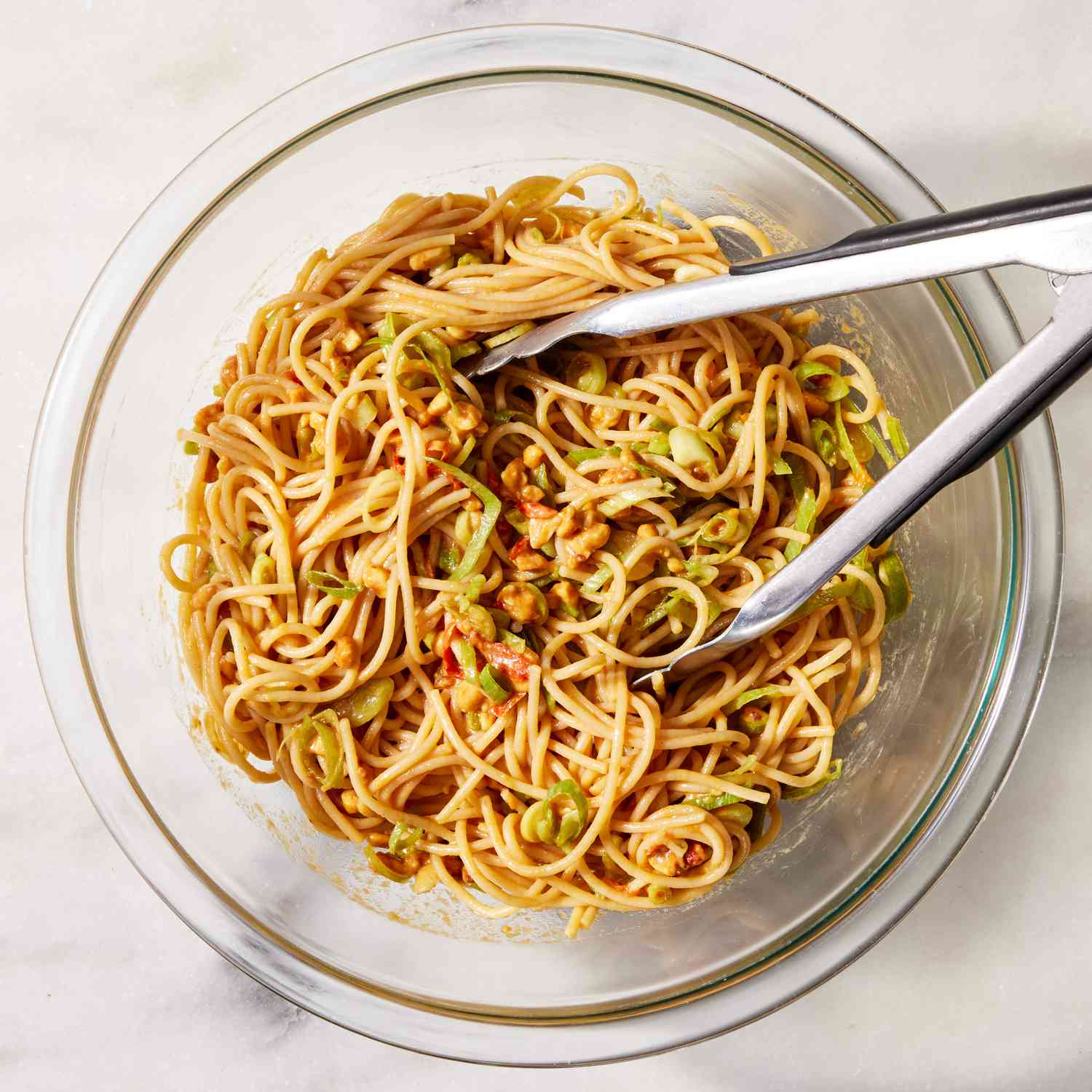 overhead view of tongs in bowl of noodles with peanut sauce
