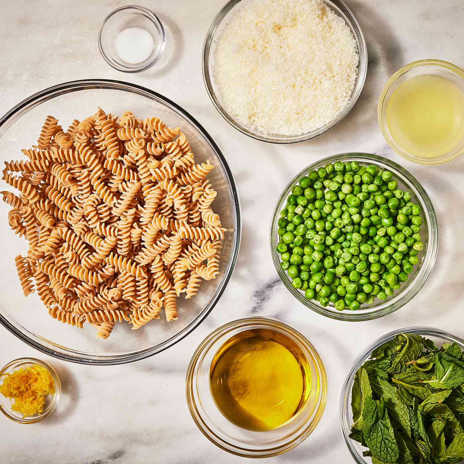 Overhead view of a ingredients in various bowls for Creamy Green Pea Pesto Pasta recipe