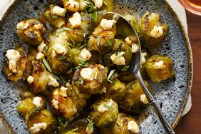 Smashed Brussels sprouts with goat cheese & hot honey in a blue and with patterned bowl, with a serving spoon
