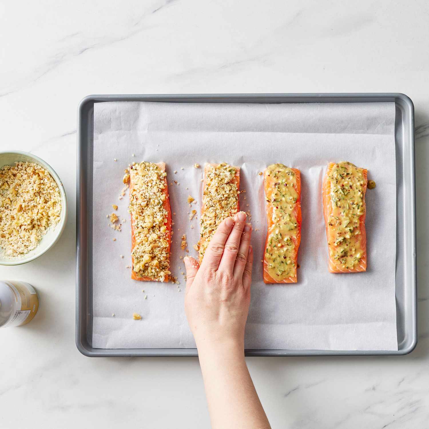 Four salmon fillets on a parchment paper covered baking sheet, getting topped with walnut rosemary topping