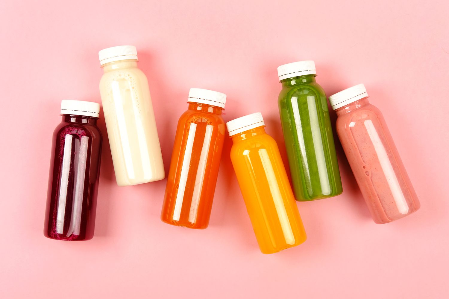 Bottles of multicolored smoothies or juices on pink background. Flat lay style.