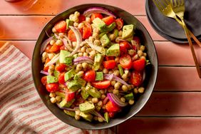 A bowl of salad with avocado, cherry tomatoes, chickpeas, and red onion on a table
