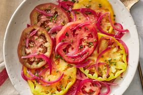Overhead view of a rustic off-white plate of Heirloom Tomato Salad with Pickled Onions recipe