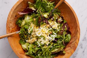 Overhead view of spoons tossing ingredients in a large wooden bowl for Chickpea, Artichoke & Avocado Salad with Apple-Cider Dressing recipe