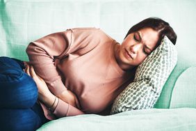 woman clutching her stomach while laying on the couch