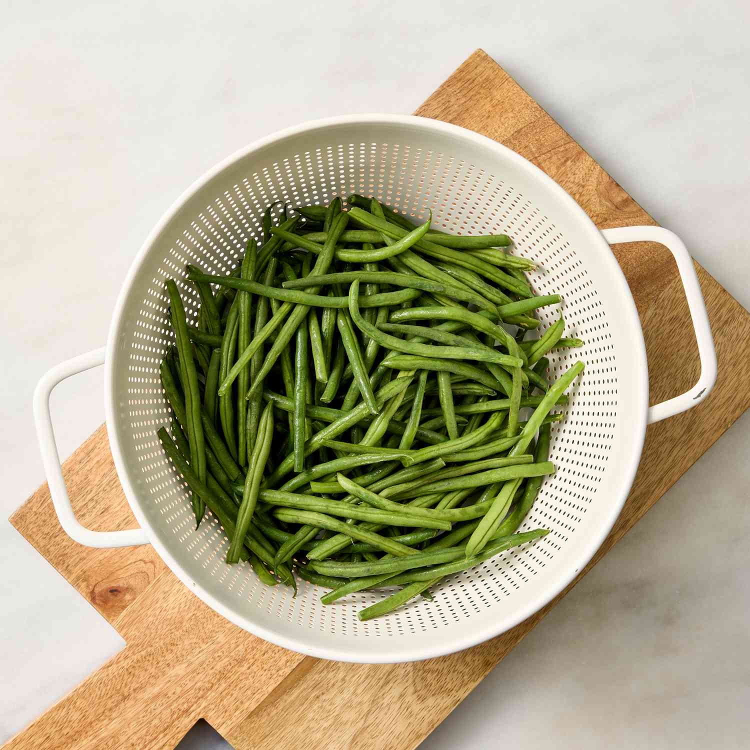 Fresh green beans in a colander on a wooden board