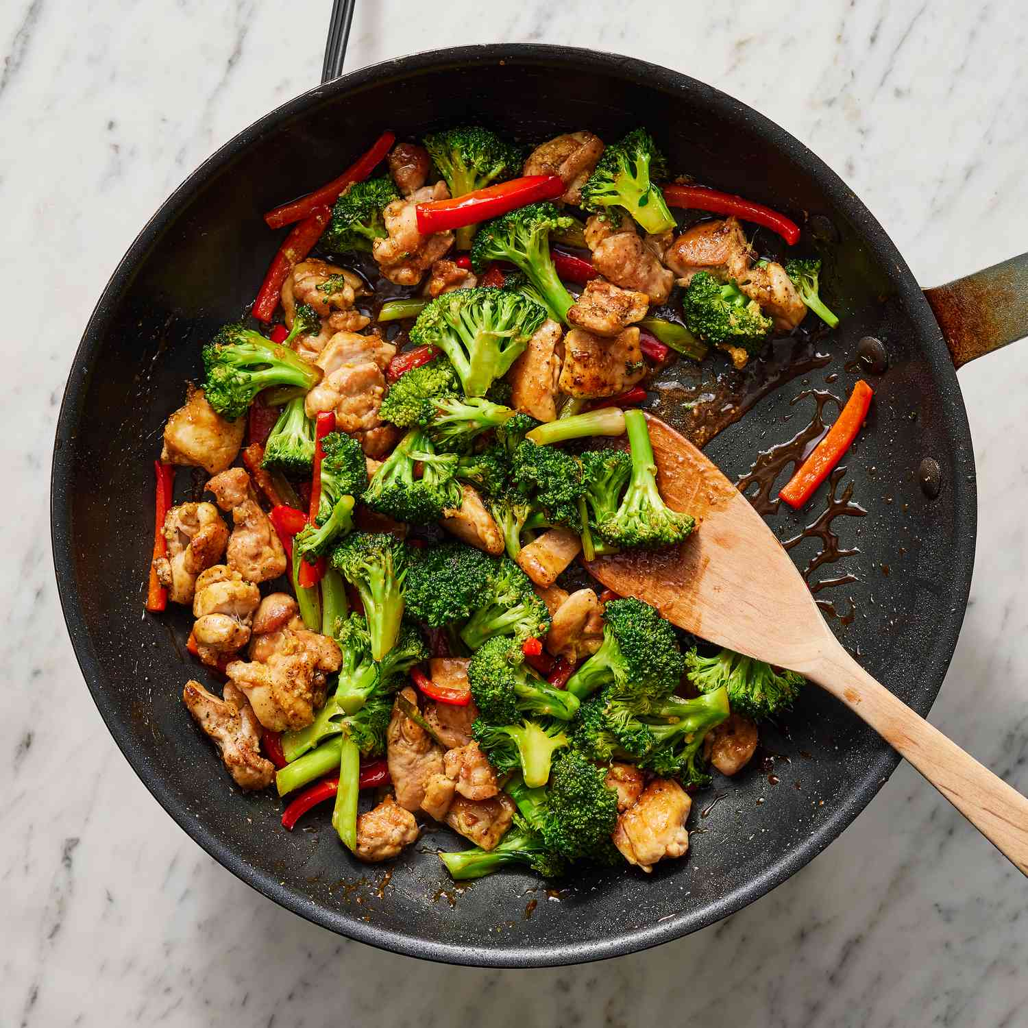 overhead view of pan with cooked chicken pieces, chopped broccoli, bell peppers, and a brown sauce