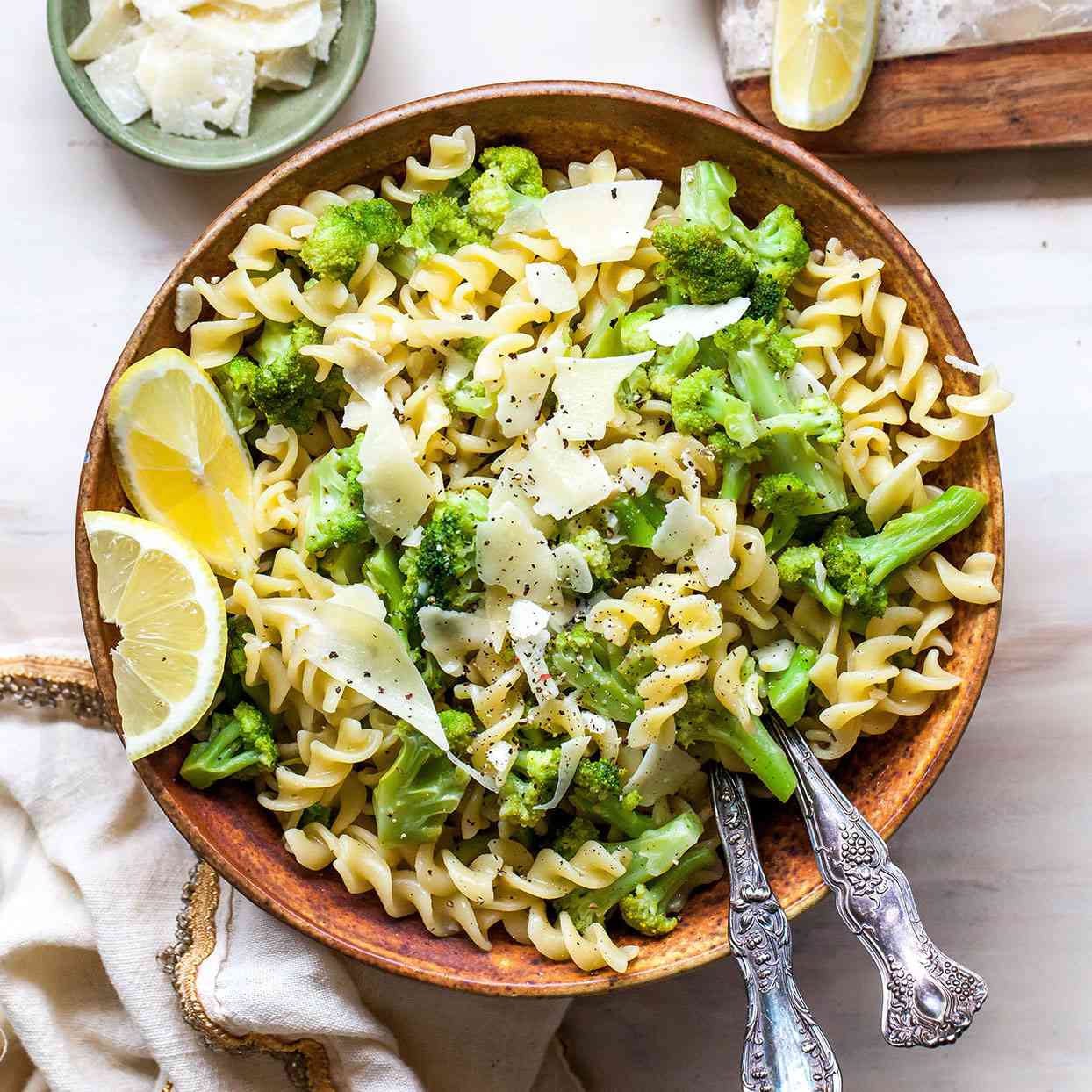 overhead shot of brown bowl filled with rotini pasta, broccoli, parmesan and lemon slices
