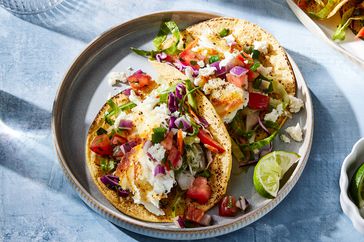  A light blue plate with two seared halibut fish tacos with cilantro slaw, garnished with lime wedges