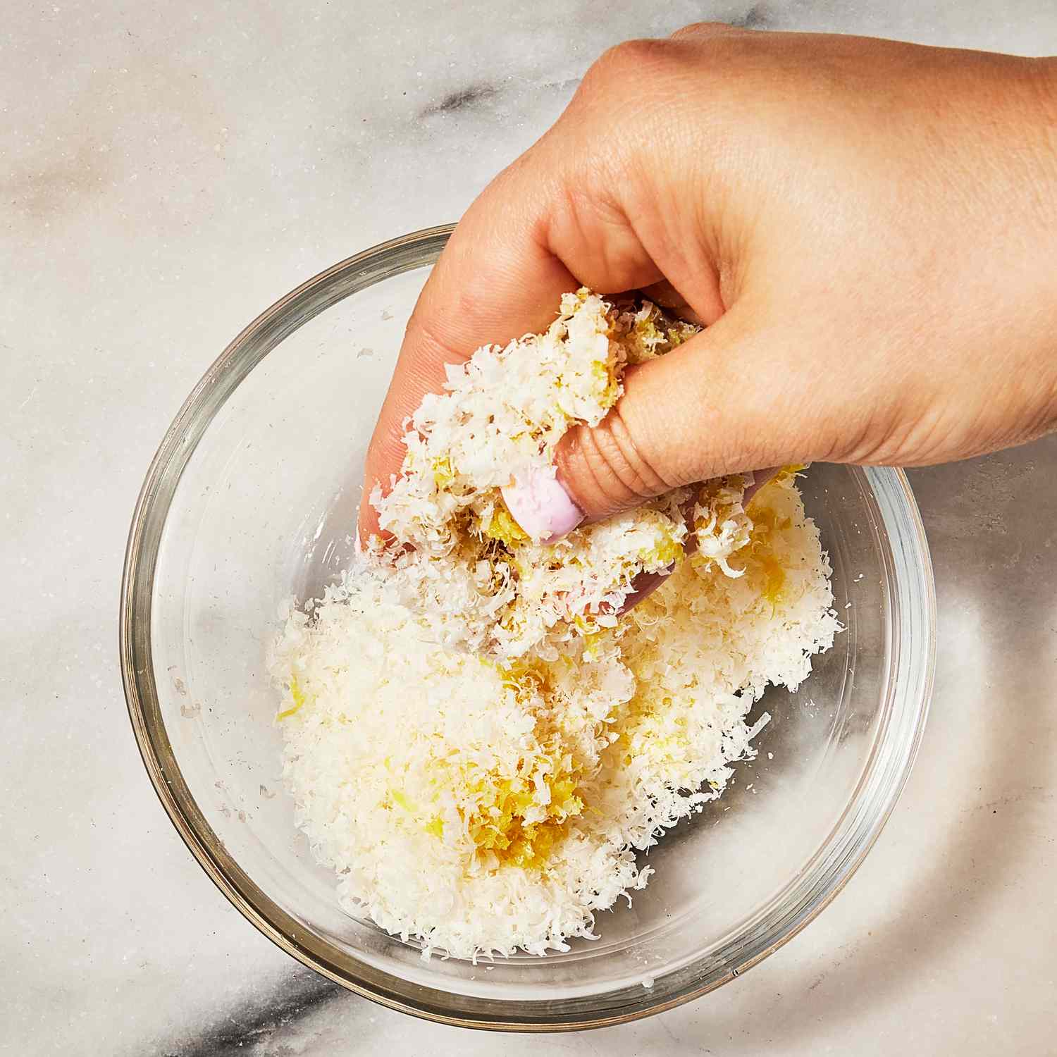 Overhead view of a hand mixing parmesan and lemon zest in a small bowl for Creamy Green Pea Pesto Pasta recipe