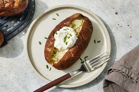 An air-fryer baked potato on a plate, topped with sour cream and chopped chives