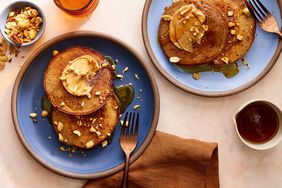 Peanut butter pancakes on a blue plate, topped with crushed mixed nuts, a schmear peanut butter and syrup