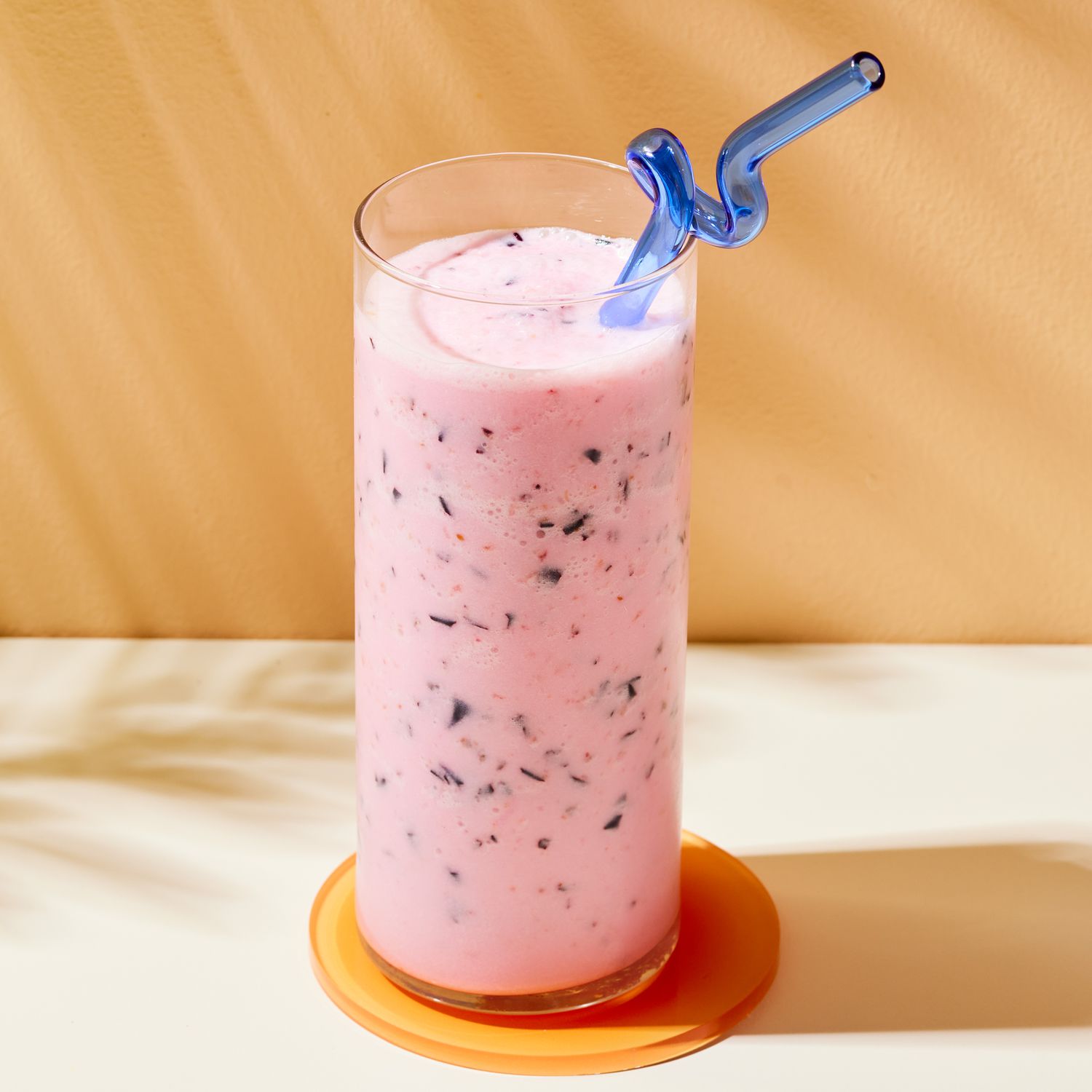 glass of pink smoothie with dark blue specs and a blue straw