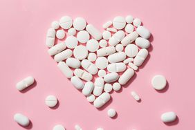 Pills arranged in a heart shape on a pink background.