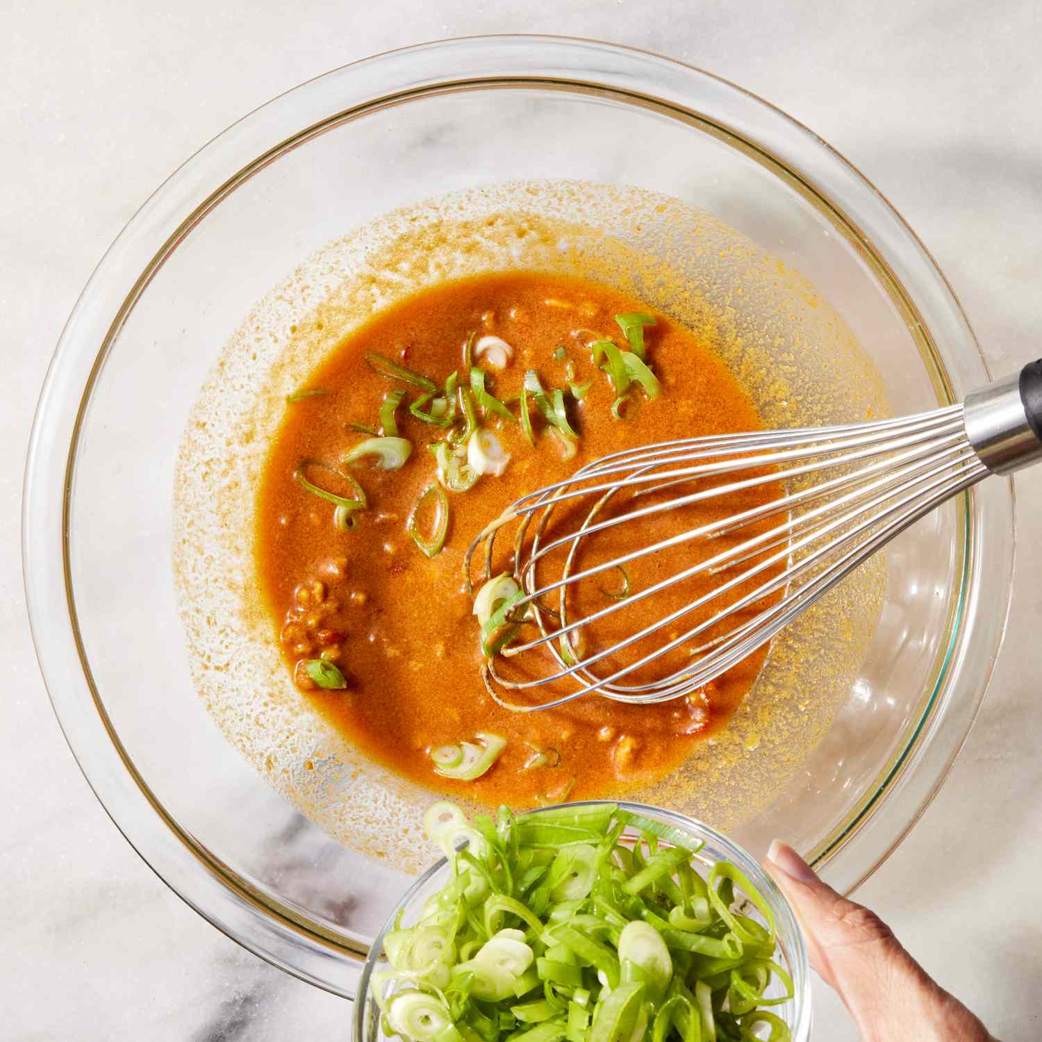 overhead view of sauce in a bowl with whisk while adding sliced scallions