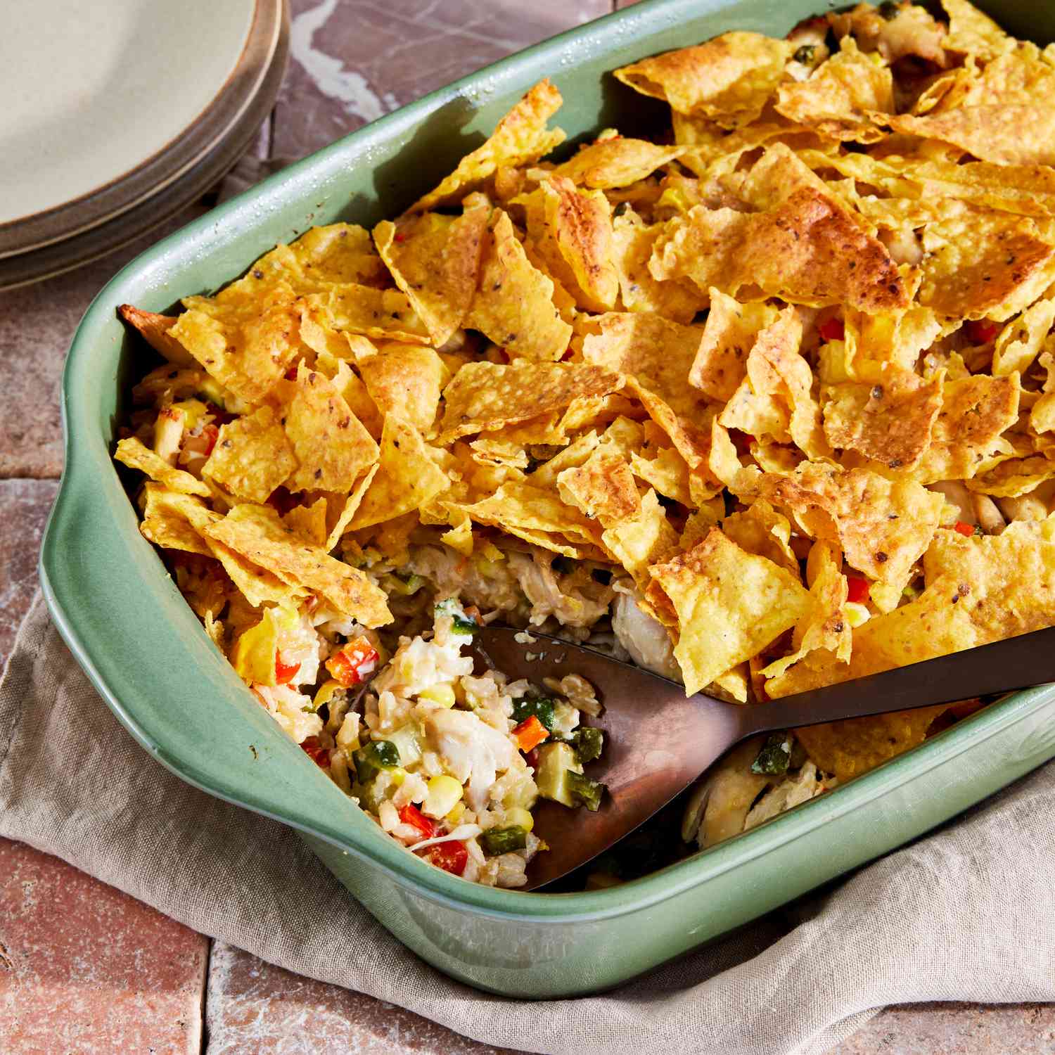 Green chile rotisserie chicken casserole recipe in a light green baking dish, with a serving spoon spooning out a portion of the casserole