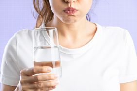 a photo of a woman gargling water while holding a glass of water