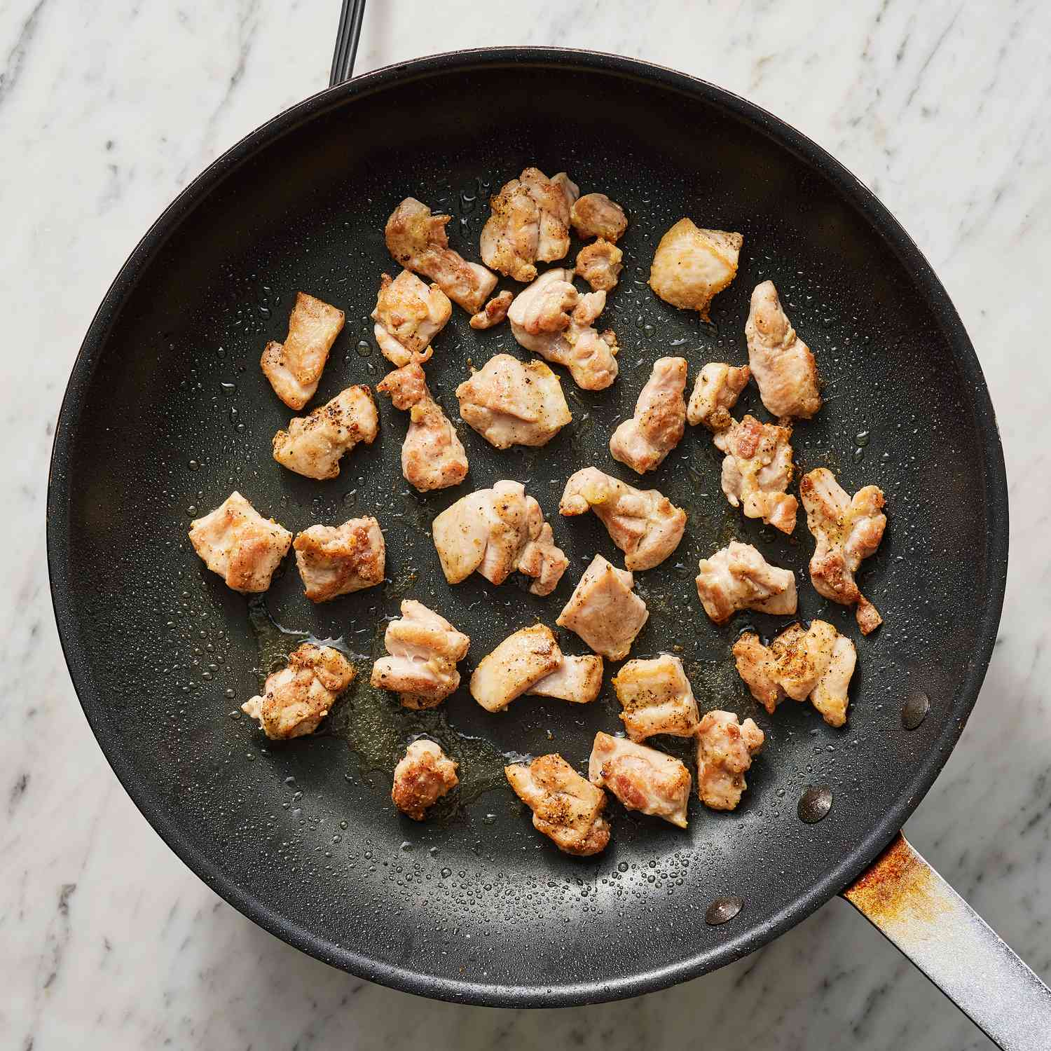 Overhead view of chicken pieces browned in a pan
