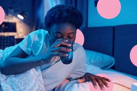 A person in bed drinking a glass of water at night, illuminated in dim blue lighting