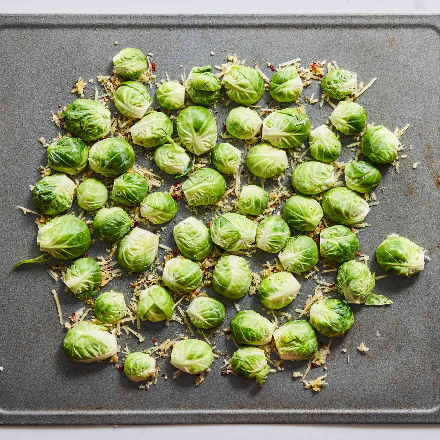 overhead view of raw halved brussels sprouts placed on top of parmesan mixture on a sheet pan