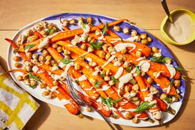 A serving plate with roasted sliced carrots, topped with a tahini sauce and crispy chickpeas