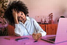 a photo of a woman looking tired at her desk and taking her glasses off 