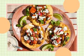 Three tostadas with vegetable toppings and garnished with drizzled sauce on a plate, accompanied by lime wedges