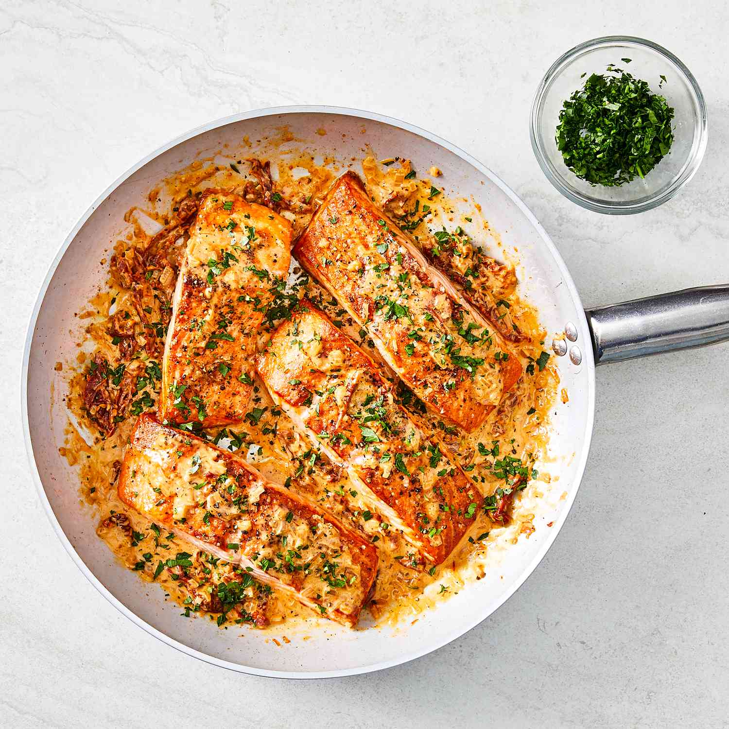 overhead view of pan with cooked salmon fillets, sauce, and herb garnish