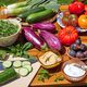 Fresh vegetables and fruits with dips displayed on a wooden table, including cucumbers, eggplants, tomatoes, figs, and greens