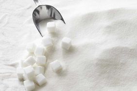 a pile of granulated sugar with a scoop and sugar cubes