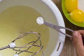 Hand of woman holding measure spoon with cream tartar to put it into egg whites before beating - stock photo