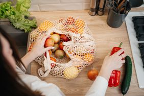 A person organizing fresh produce like apples and peppers on a kitchen counter