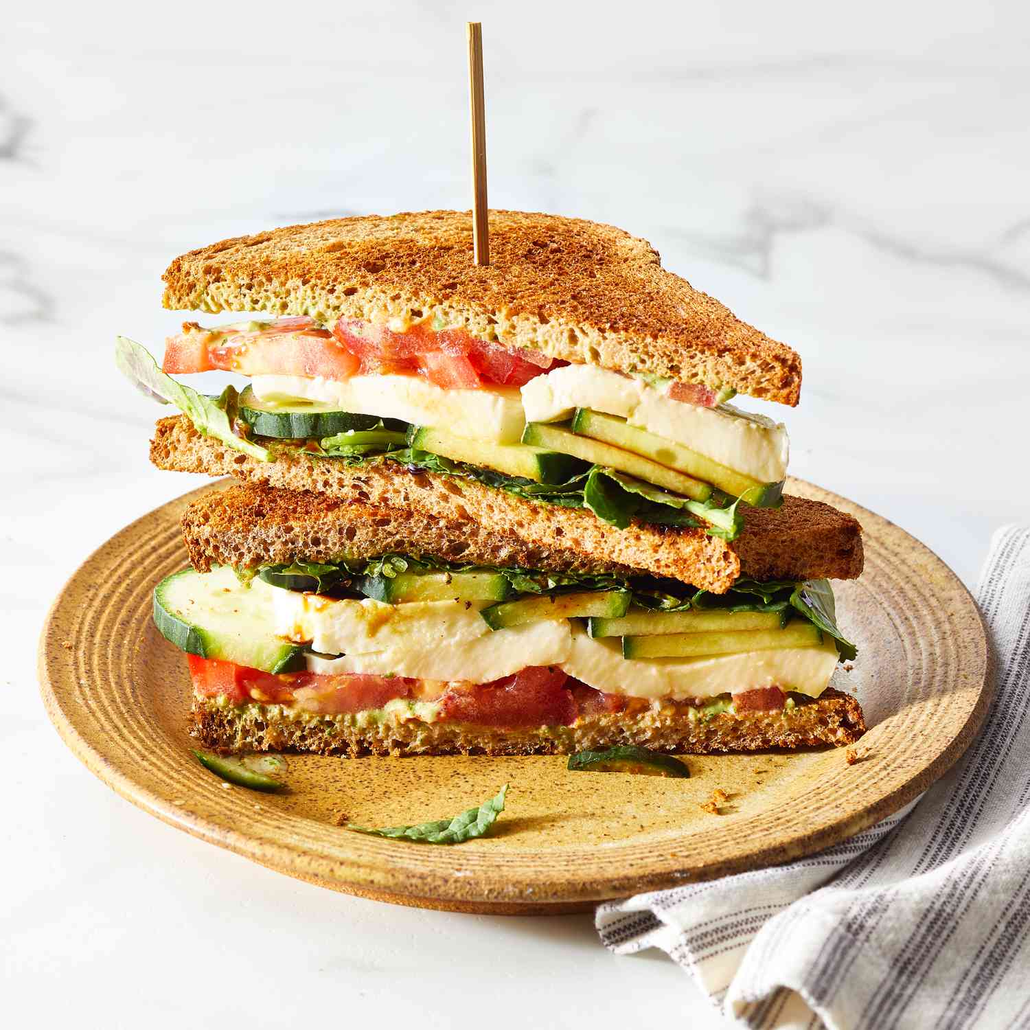 Angle view of 2 halves of a Cucumber Caprese Sandwich recipe stacked on a brown stoneware plate