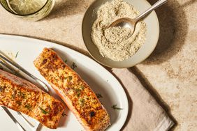 Overhead view of a bowl of seasoning mix in a bowl with a spoon next to a plate of salmon fillets