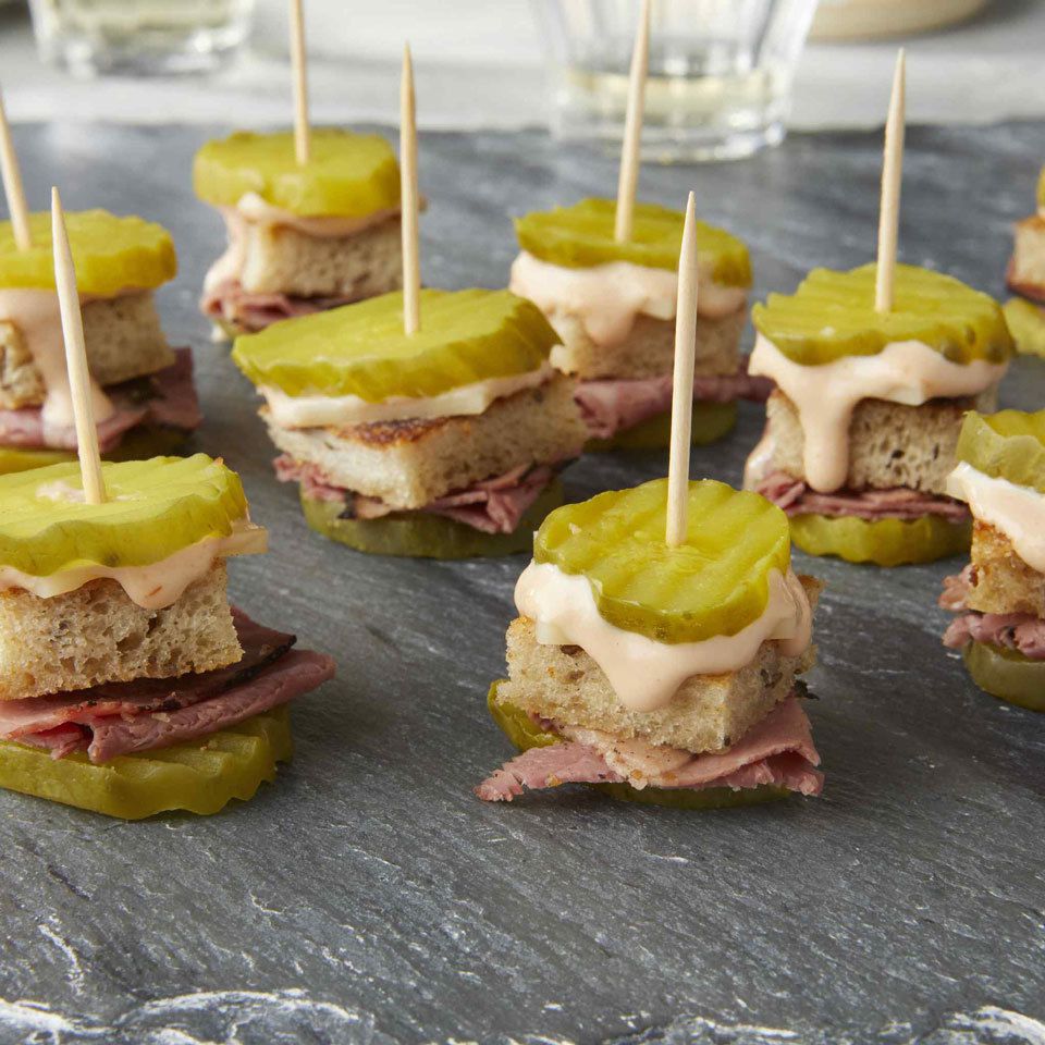 stacks of pickles, bread, pastrami and cheese with a toothpick