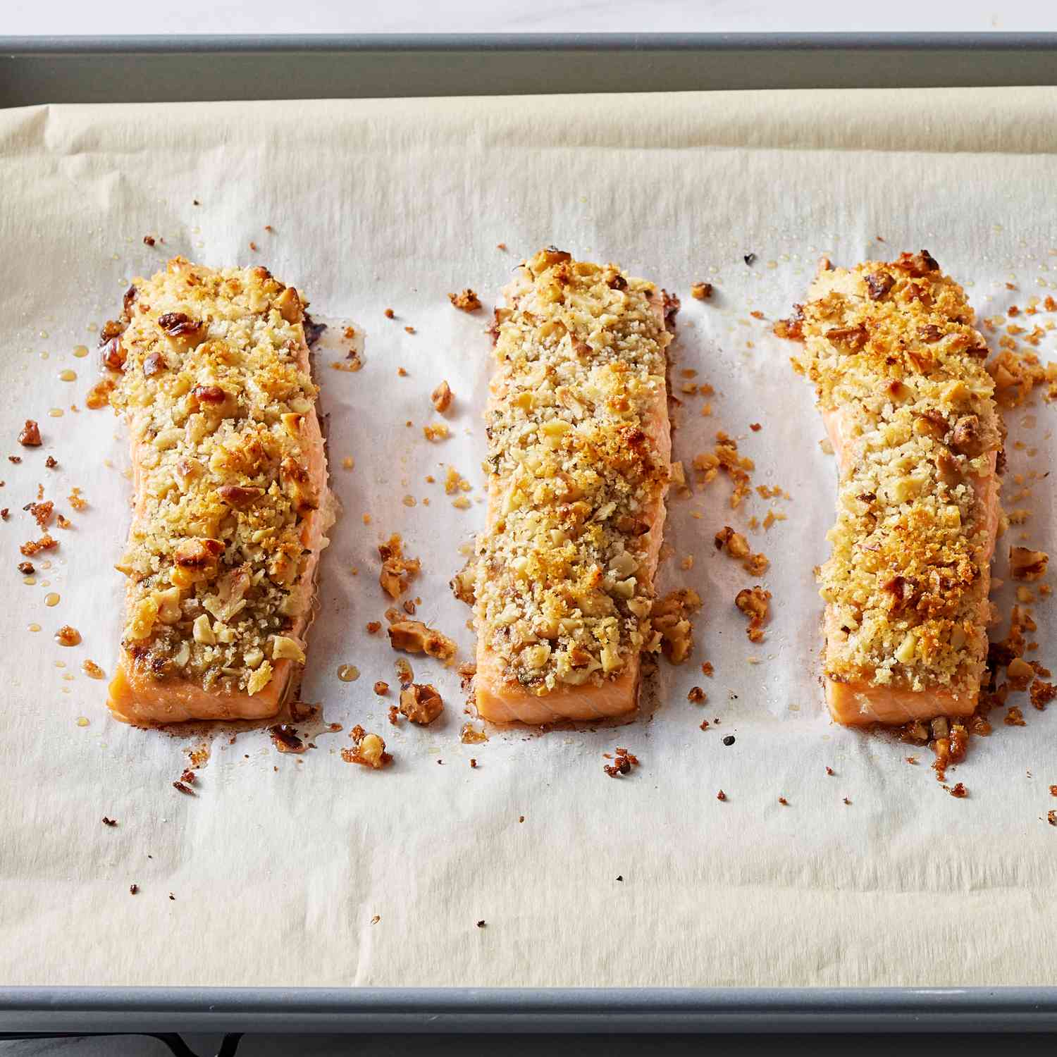 Three salmon fillets for the walnut-rosemary crusted salmon recipe, baked on a parchment paper covered baking sheet