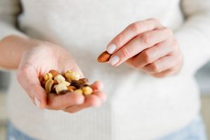 A person holding various nuts in one hand and picking one with the other, demonstrating the consumption of healthy snacks