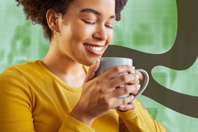 A person smiling and holding a mug near their face against a green background