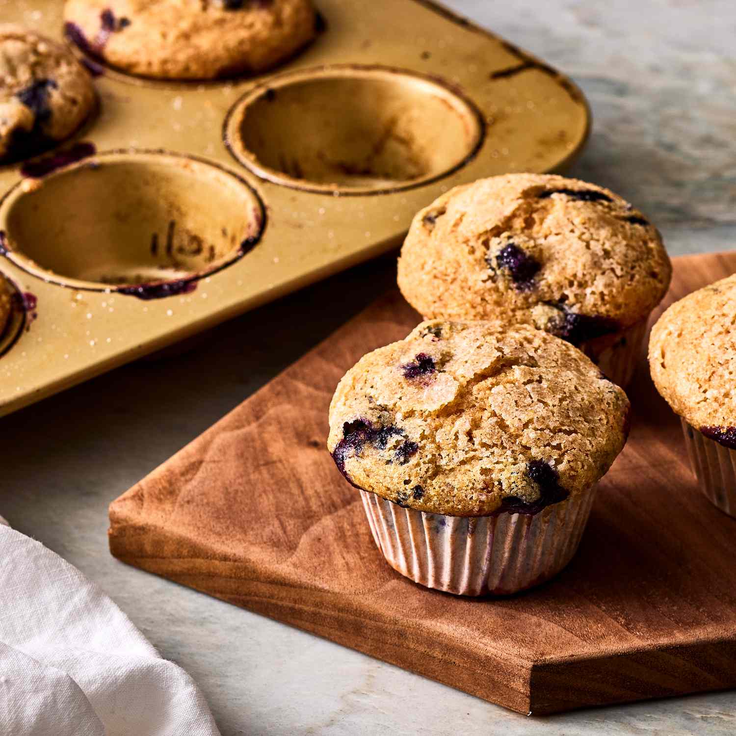 cooked blueberry muffins on a serving board and a muffin tin in the background