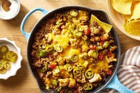 Cheesy ground beef & cauliflower casserole recipe with one tortilla chip scooping casserole out, a bowl of more chips is on the side of the casserole skillet