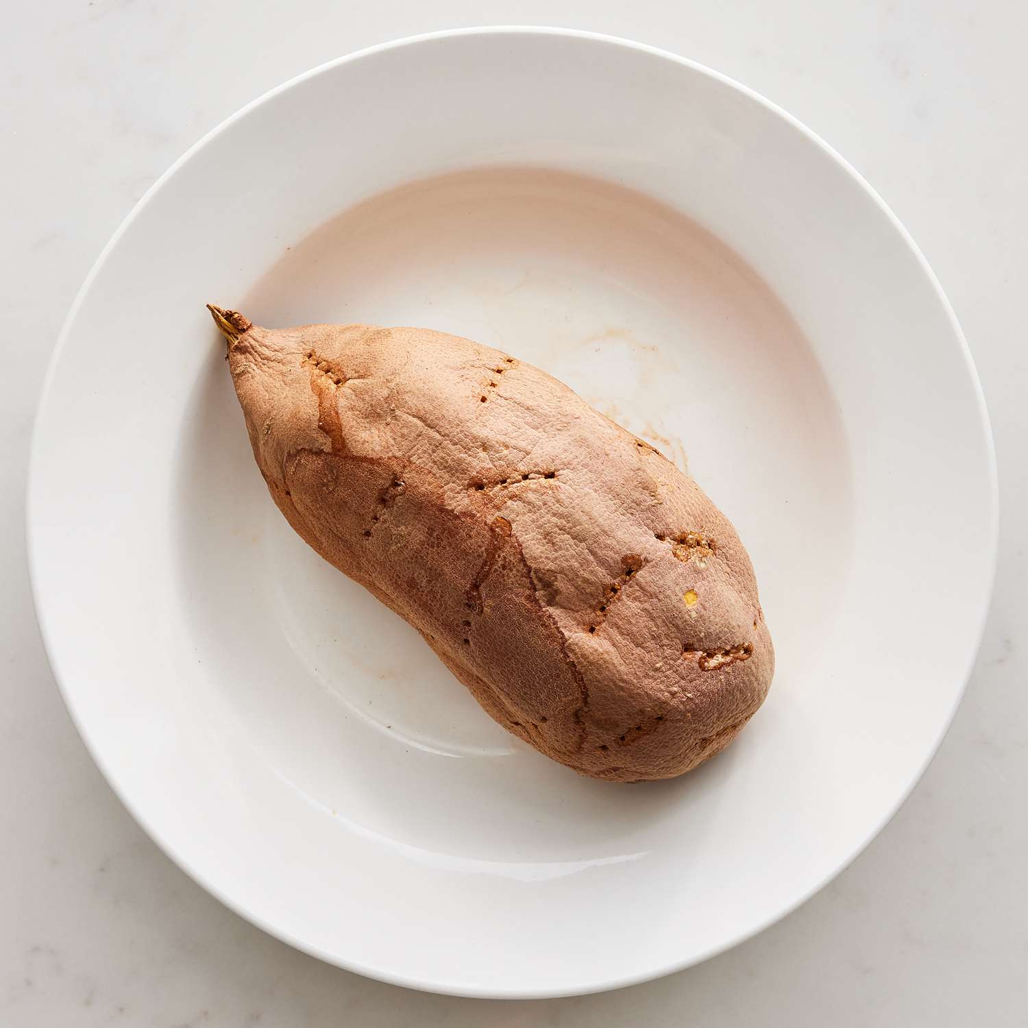 Overhead view of a cooked sweet potato on a white plate from Maple-Cinnamon Sweet Potato Bread recipe