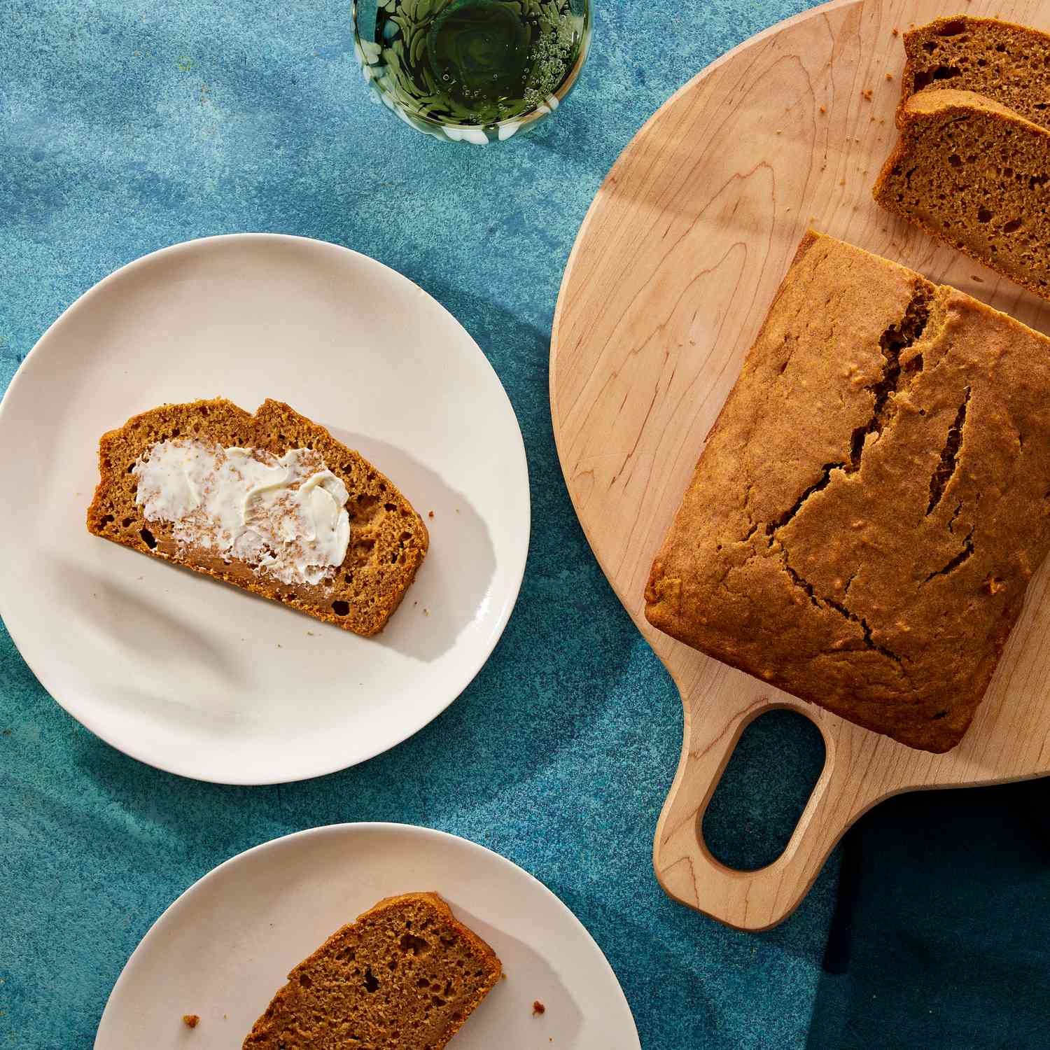 Overhead view of a slice of Maple-Cinnamon Sweet Potato Bread recipe on a white plate and a partially sliced loaf on a wooden cutting board