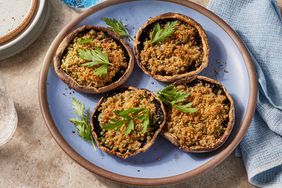 Four roasted bread-crumb filled portobello caps on a light blue plate, garnished with fresh parsley