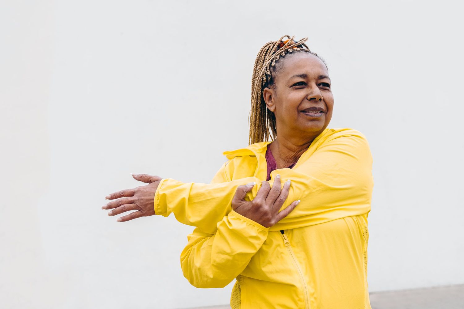 African senior woman doing workout routine while stretching outdoor - Focus on face