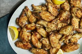 a recipe photo of the Crispy Oven-Baked Lemon-Pepper Chicken Wings on a platter served with lemons beside them