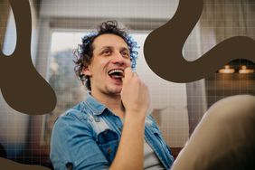 A person seated indoors, eating food and smiling