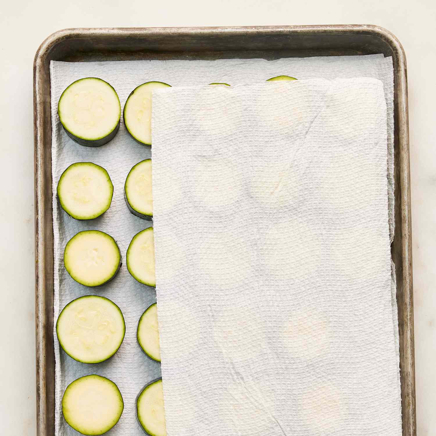 zucchini rounds on a baking sheet with paper towel partially covering them